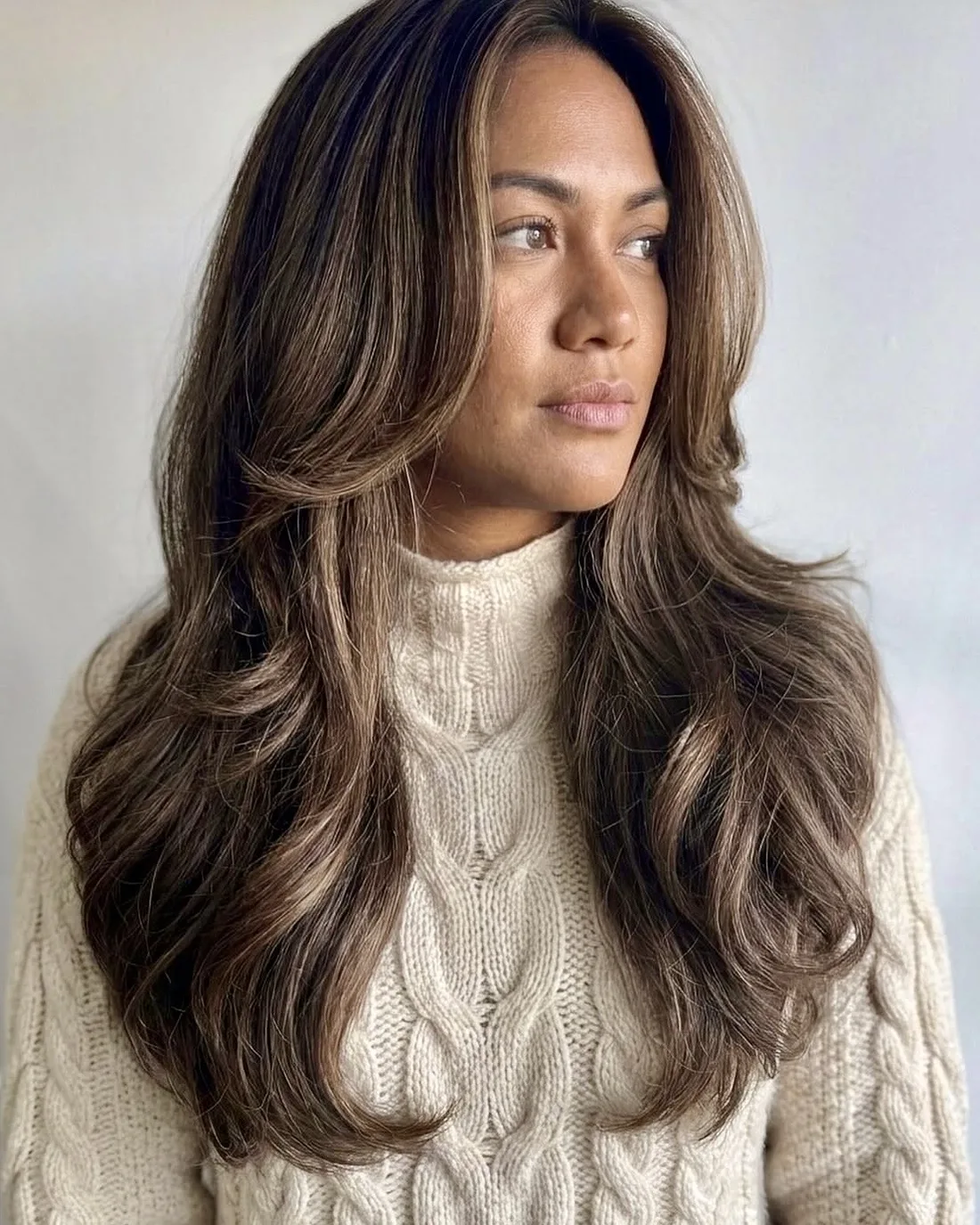 Woman with long, layered dark brown hair and soft caramel face-framing pieces after a blow-dry at HEADS Salon